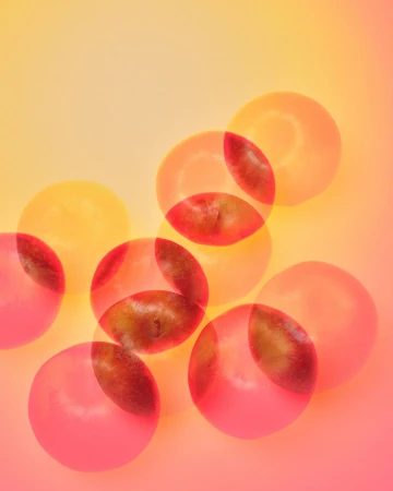 Overlapping semi-transparent grapes in shades of orange, pink, and red on a warm-toned gradient background create a playful, abstract composition.