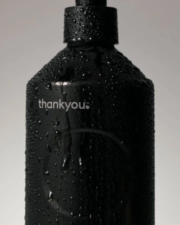 Close-up of a black plastic bottle covered in water droplets against a plain grey background, featuring the brand name 'thankyou.'.