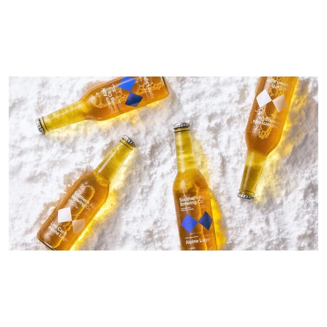 Overhead shot of four bottles of golden Alpine Lager from Southern Brewing Company resting on a powdery white background.