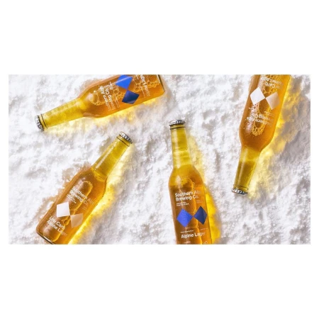 Overhead shot of four bottles of golden Alpine Lager from Southern Brewing Company resting on a powdery white background.