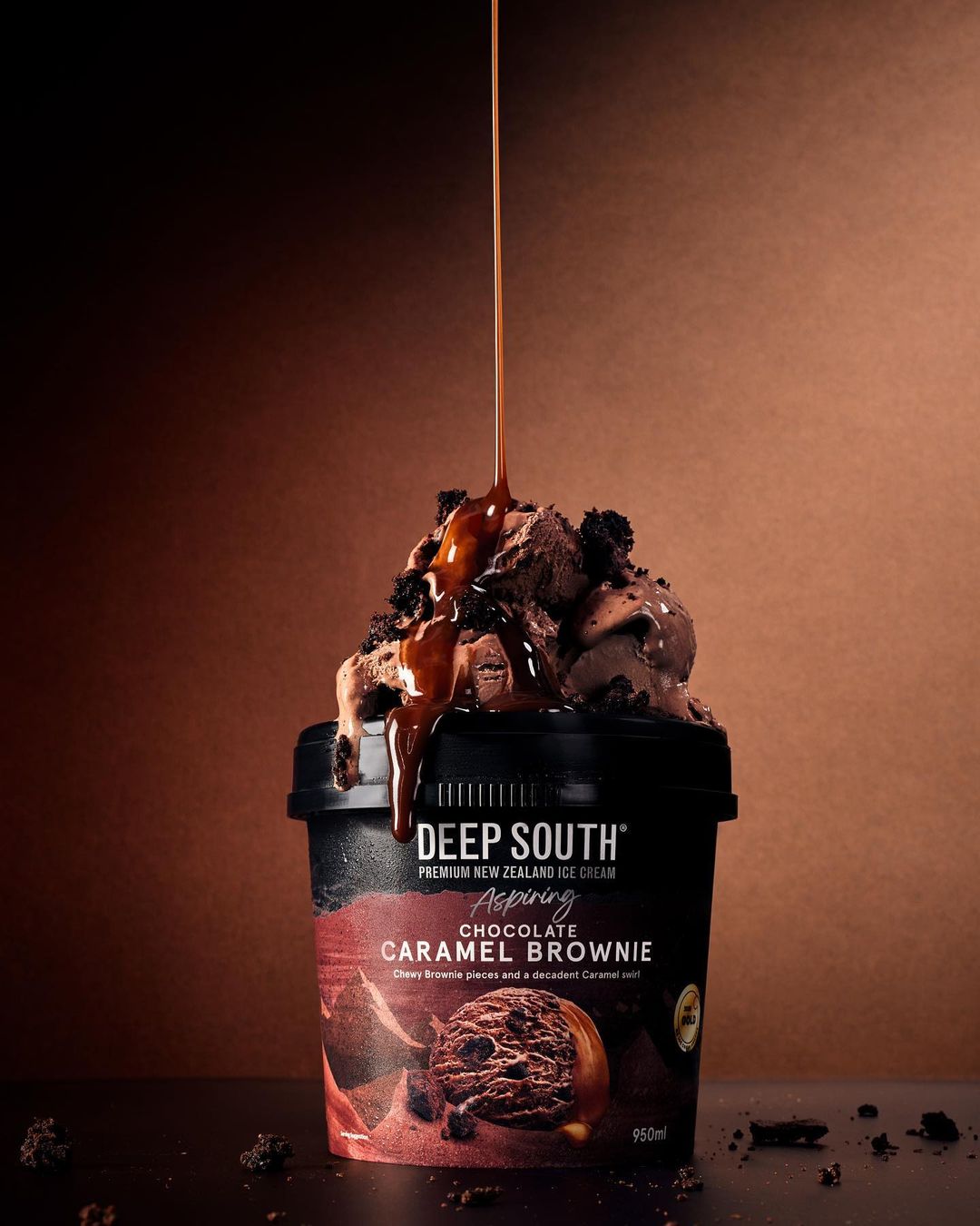 Pouring caramel on chocolate brownie ice cream in a black container. Decadent dessert with rich color grading and studio lighting.