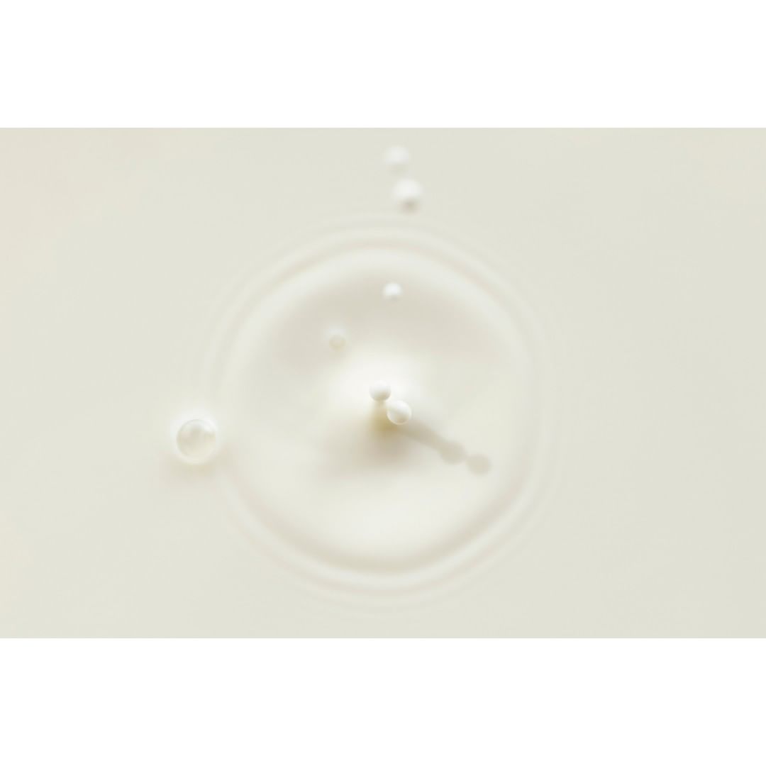 Close-up of a splash of white liquid with droplets and ripples forming a circular pattern on a light-colored surface, food photography.