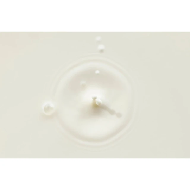 Close-up of a splash of white liquid with droplets and ripples forming a circular pattern on a light-colored surface, food photography.