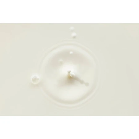Close-up of a splash of white liquid with droplets and ripples forming a circular pattern on a light-colored surface, food photography.