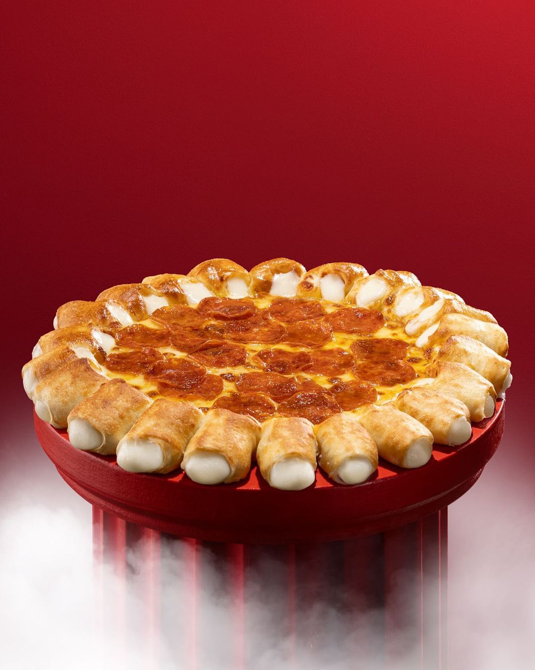 A pepperoni pizza with stuffed cheese crust on a red plate, presented against a gradient dark-red background with diffused lighting.
