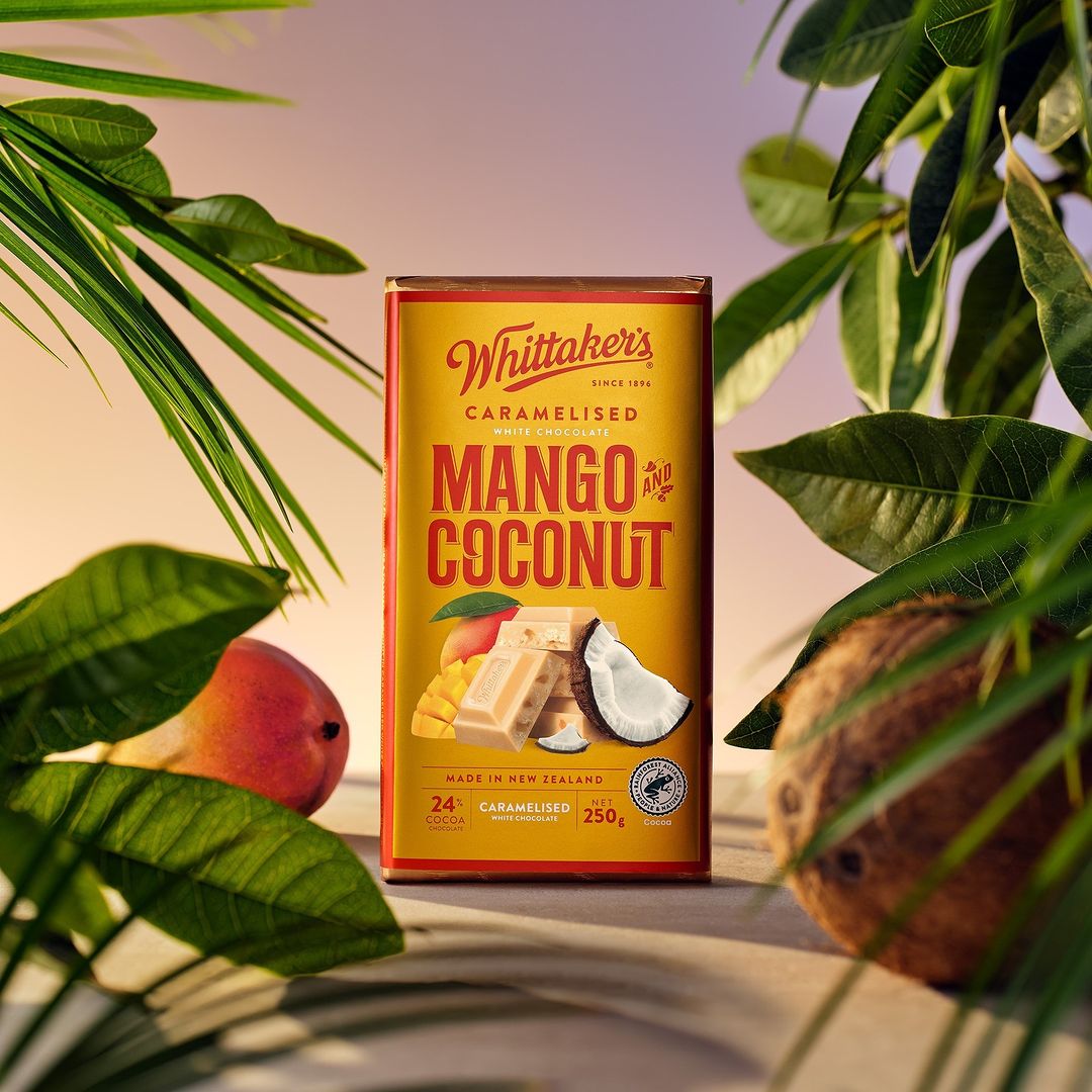 Whittaker's Caramelised Mango and Coconut white chocolate bar in packaging with mango, coconut, and green leaves.