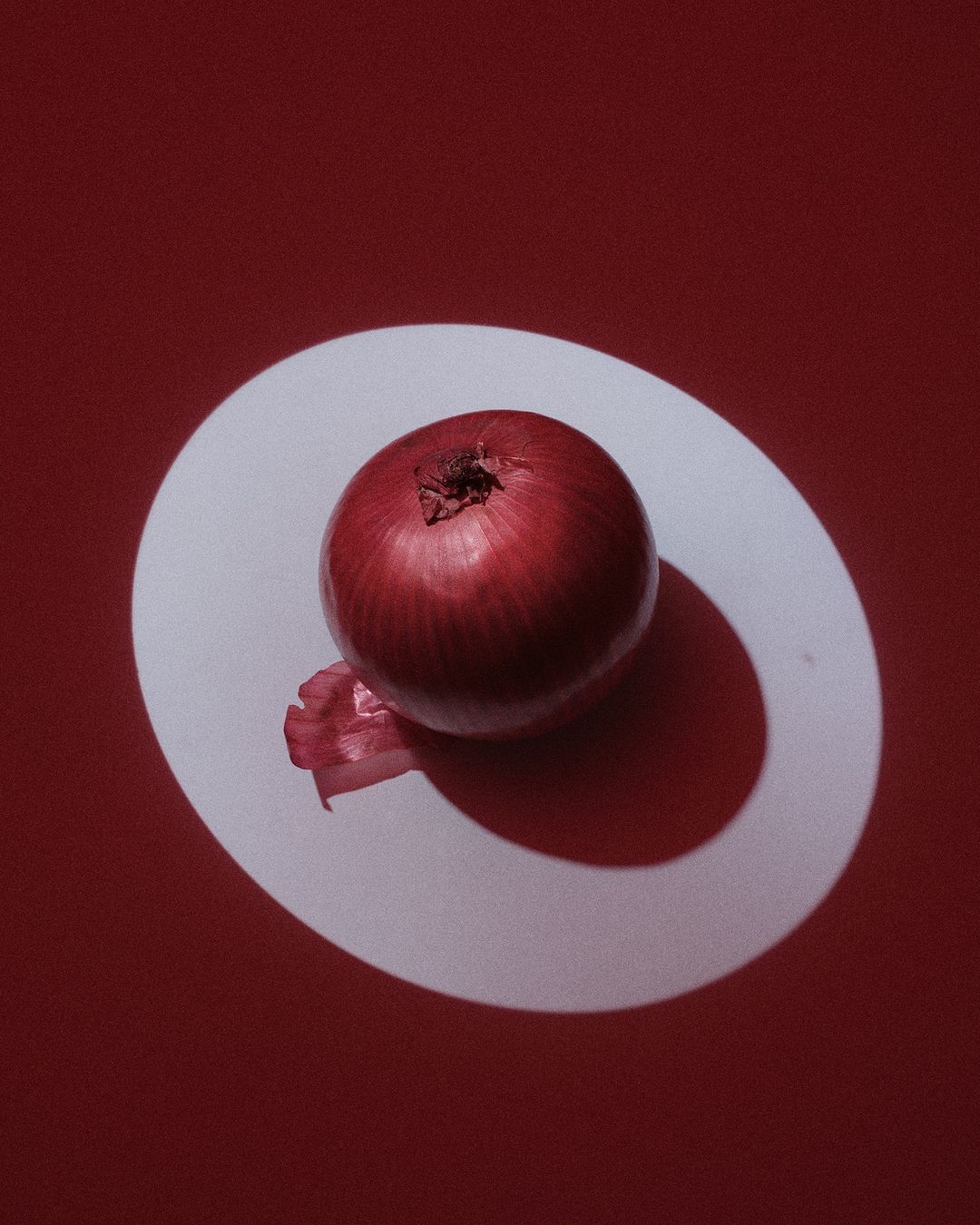 Studio shot of a red onion on a white surface against a red background, showcasing food photography with strong shadows and a clean aesthetic.