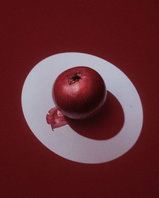 Studio shot of a red onion on a white surface against a red background, showcasing food photography with strong shadows and a clean aesthetic.
