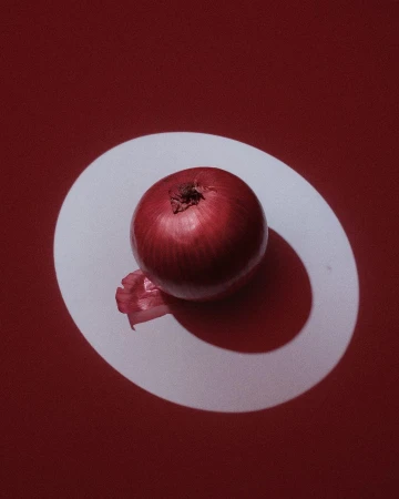 Studio shot of a red onion on a white surface against a red background, showcasing food photography with strong shadows and a clean aesthetic.