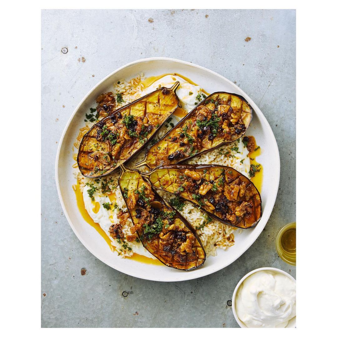 Overhead shot of a plate with four halves of grilled eggplant on a bed of rice, topped with herbs and a sauce drizzle.