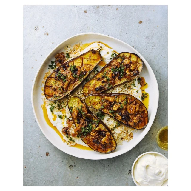 Overhead shot of a plate with four halves of grilled eggplant on a bed of rice, topped with herbs and a sauce drizzle.
