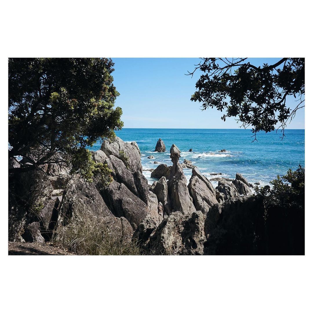 Seascape view featuring rock formations, vegetation, and turquoise ocean waters under a clear blue sky, captured in natural light.