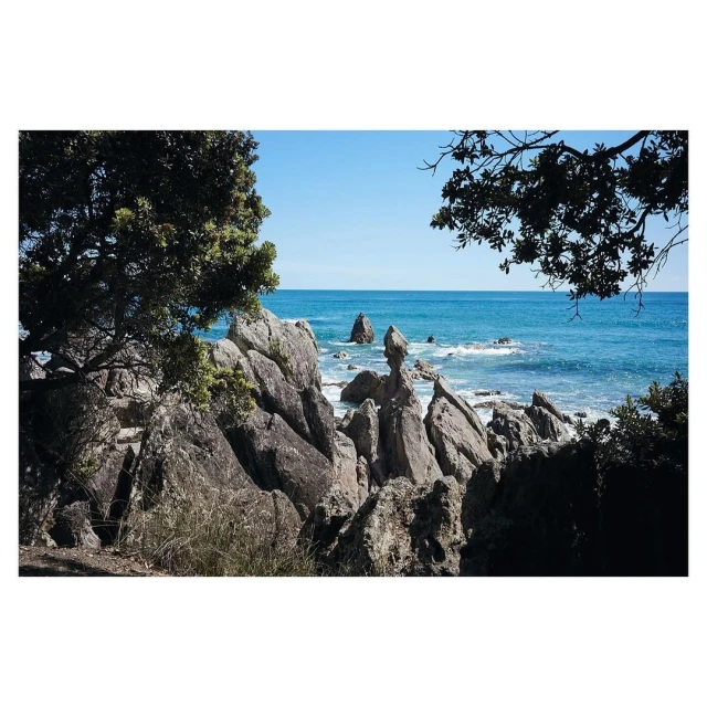 Seascape view featuring rock formations, vegetation, and turquoise ocean waters under a clear blue sky, captured in natural light.