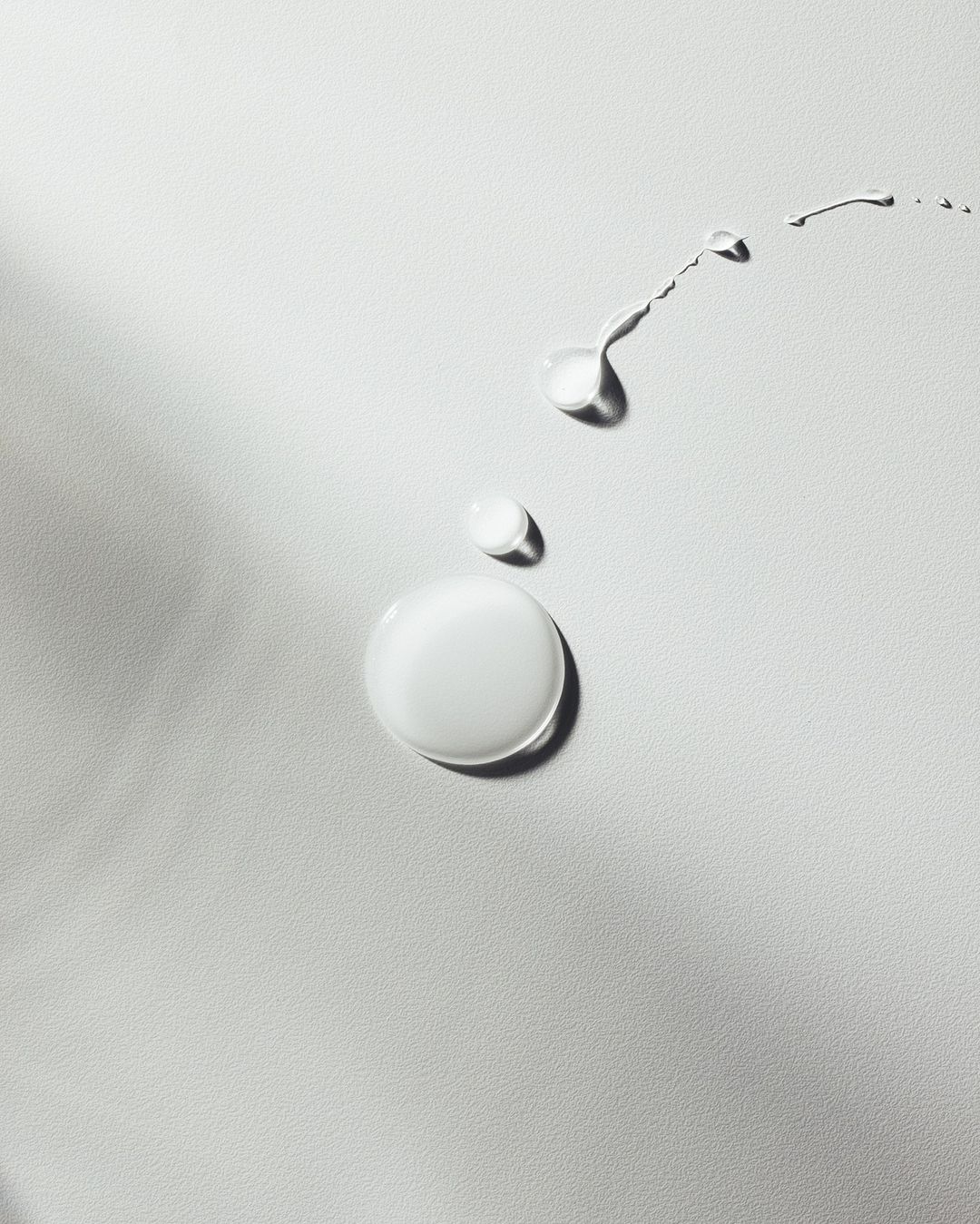 Close-up studio shot of drops and trails of liquid, glossy fluid on white surface, product shot, beauty, skincare concept.