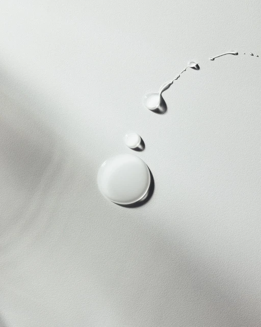 Close-up studio shot of drops and trails of liquid, glossy fluid on white surface, product shot, beauty, skincare concept.