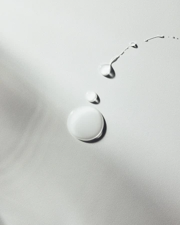 Close-up studio shot of drops and trails of liquid, glossy fluid on white surface, product shot, beauty, skincare concept.