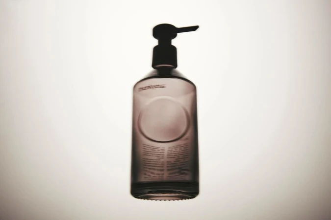 Studio shot of a dark glass bottle with a pump dispenser against a bright white background, emphasizing its simple design and functionality.