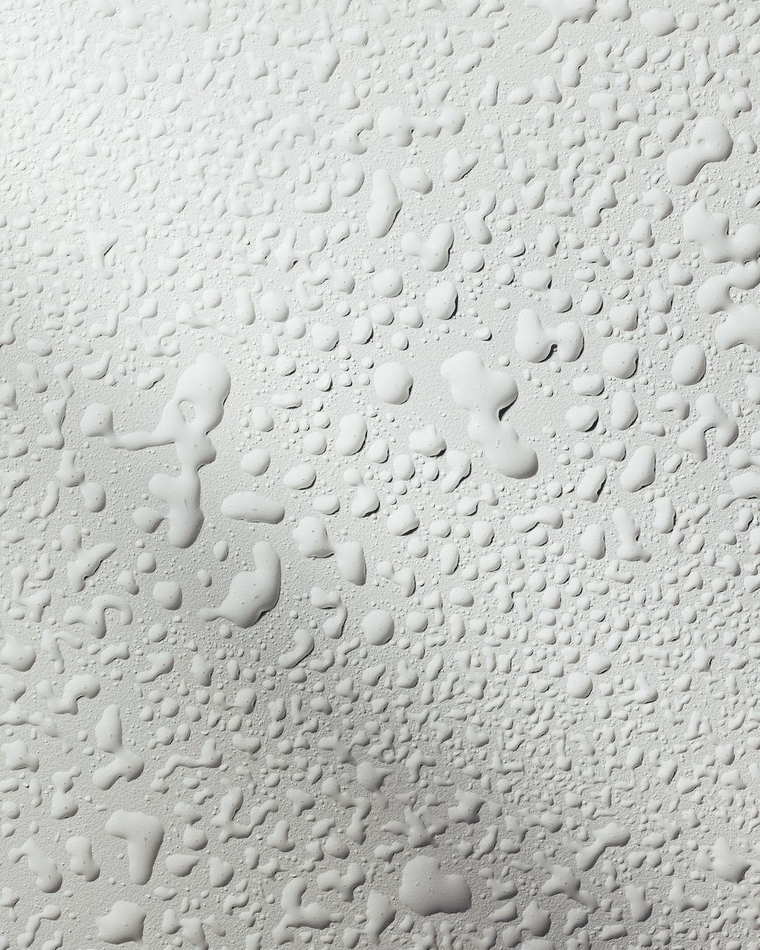 Close-up shot of water droplets on a light gray surface, creating a textured, abstract pattern with varied sizes and shapes.