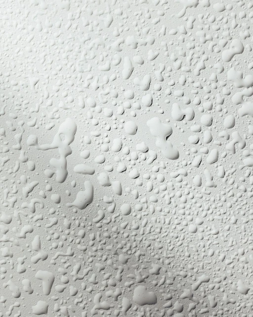 Close-up shot of water droplets on a light gray surface, creating a textured, abstract pattern with varied sizes and shapes.