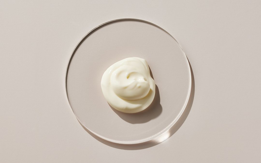 Overhead shot of white cream swirl on a round transparent plate, showcasing creamy texture and minimalist aesthetic.