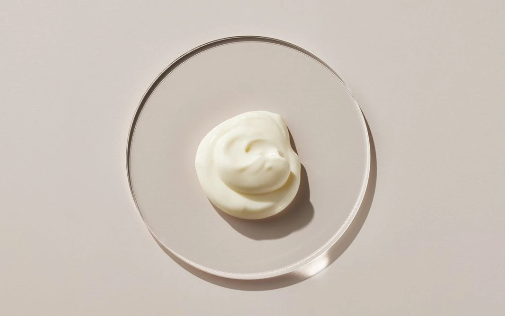 Overhead shot of white cream swirl on a round transparent plate, showcasing creamy texture and minimalist aesthetic.