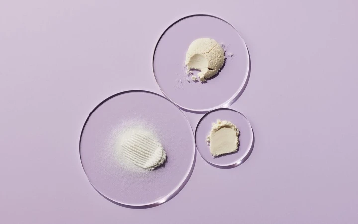 Overhead shot of skincare powders on clear acrylic discs against a soft purple backdrop, suitable for beauty and wellness product presentation.