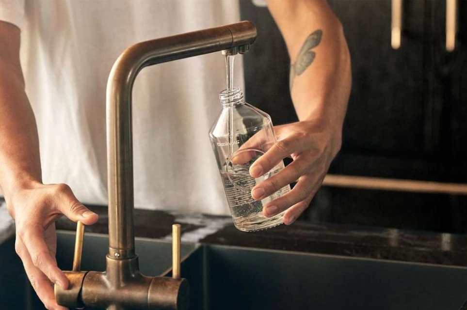 Person filling a clear bottle with water from a bronze faucet in an indoor kitchen, showcasing domestic life and clean water usage.