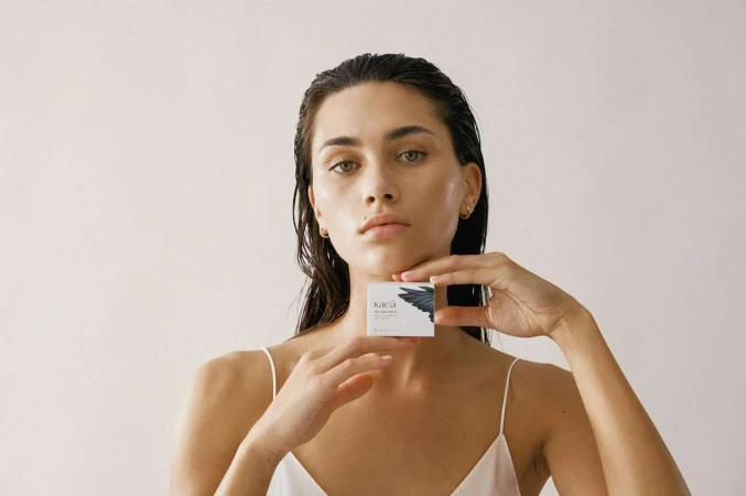 Close-up of a young woman with wet hair holding a small box in a studio setting, showcasing beauty and skincare product. 