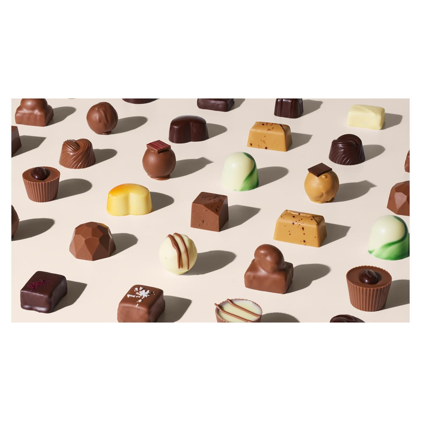 Overhead studio shot of an array of artisan chocolate candies with various shapes, colors, and textures on a light beige background.