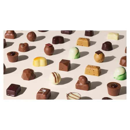 Overhead studio shot of an array of artisan chocolate candies with various shapes, colors, and textures on a light beige background.