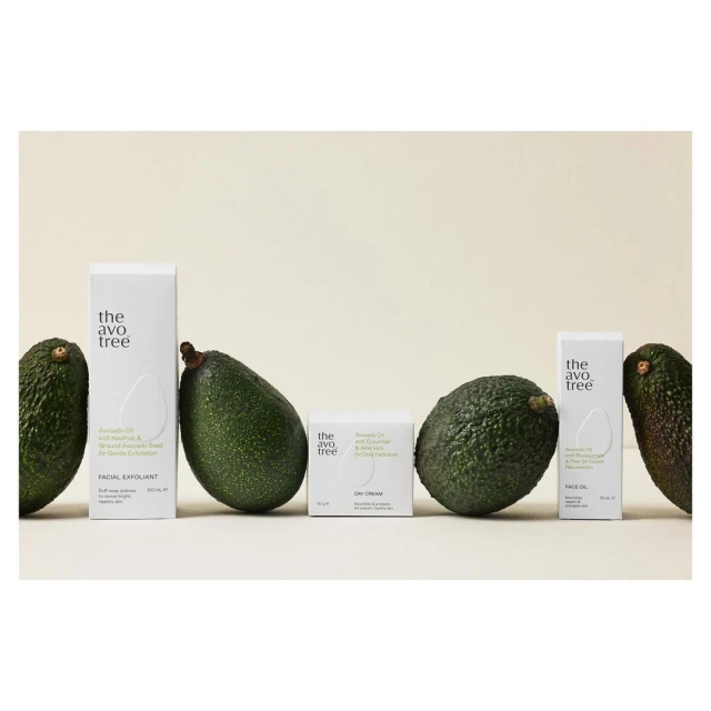 Close-up product shot of The Avo Tree skincare line featuring facial exfoliant, day cream, and face oil, accented by fresh avocados.