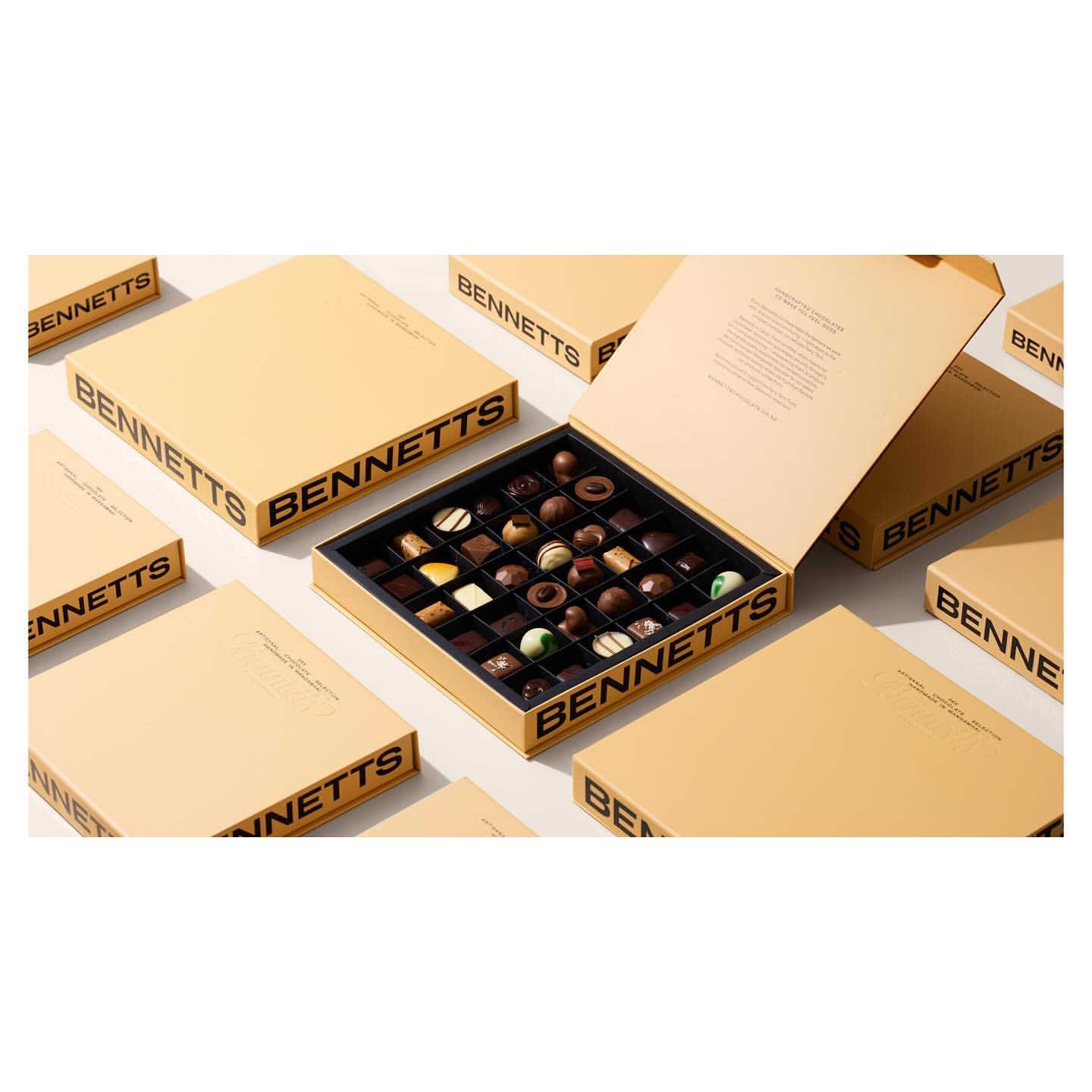 Gourmet chocolate box with an assortment of milk chocolate truffles and dark chocolate pieces surrounded by unopened boxes.