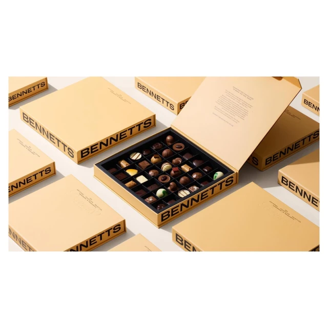 Gourmet chocolate box with an assortment of milk chocolate truffles and dark chocolate pieces surrounded by unopened boxes.