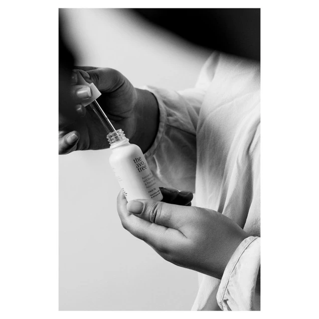 Close-up studio shot in black and white of hands holding a bottle of serum with a dropper, highlighting beauty and self-care.