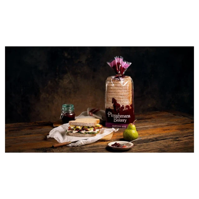 Rustic food scene featuring a sandwich, bread, jam, and pear on a wooden table against a dark backdrop. Food and Beverage still life.