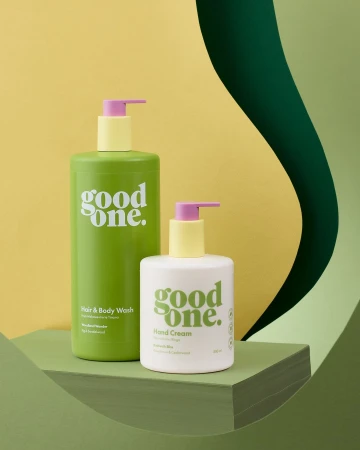 Still life shot of Good One brand hair and body wash and hand cream bottles with pastel pumps against a green and yellow background.
