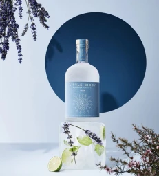 Little Biddy gin bottle perched on a clear ice block with lavender and lime on a blue background