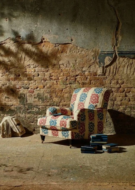 Armchair with floral pattern in aged room, illuminated by natural light, creating a vintage and cozy atmosphere.
