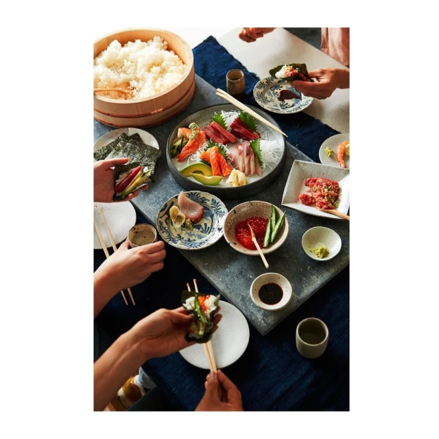 Overhead shot of a group of people enjoying a Japanese meal with sushi, sashimi, and rice on a table with ceramic dishes and chopsticks.
