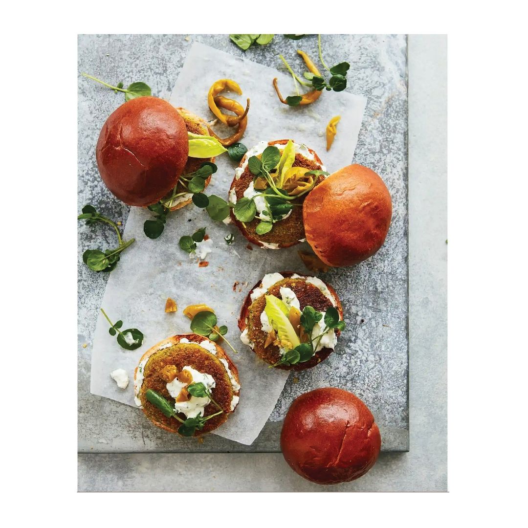 Overhead shot of gourmet vegan chickpea sliders served open-faced on brioche buns, topped with sprouts, sauce, and set on parchment.