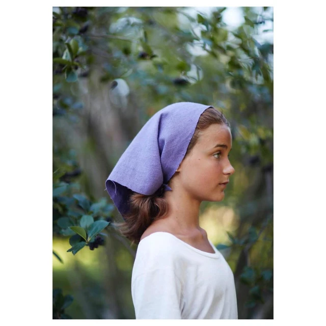 Profile shot of a teenage girl outdoors wearing a lavender headscarf and white t-shirt, with a leafy green background.