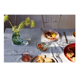 Overhead food photography of a set dining table with plates, glasses, cutlery, and a glass vase with green flowers.