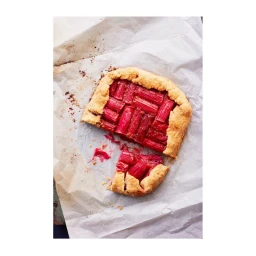 A rustic rhubarb galette sits on crumpled parchment paper with a single slice detached.