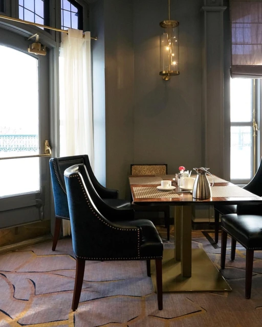 A dining area features chairs with dark blue velvet upholstery, a table set for a meal, and a modern brass hanging light fixture.