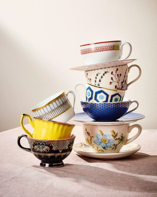 Stack of decorative tea cups and saucers with various patterns including floral and geometric designs, photographed indoors with soft lighting.