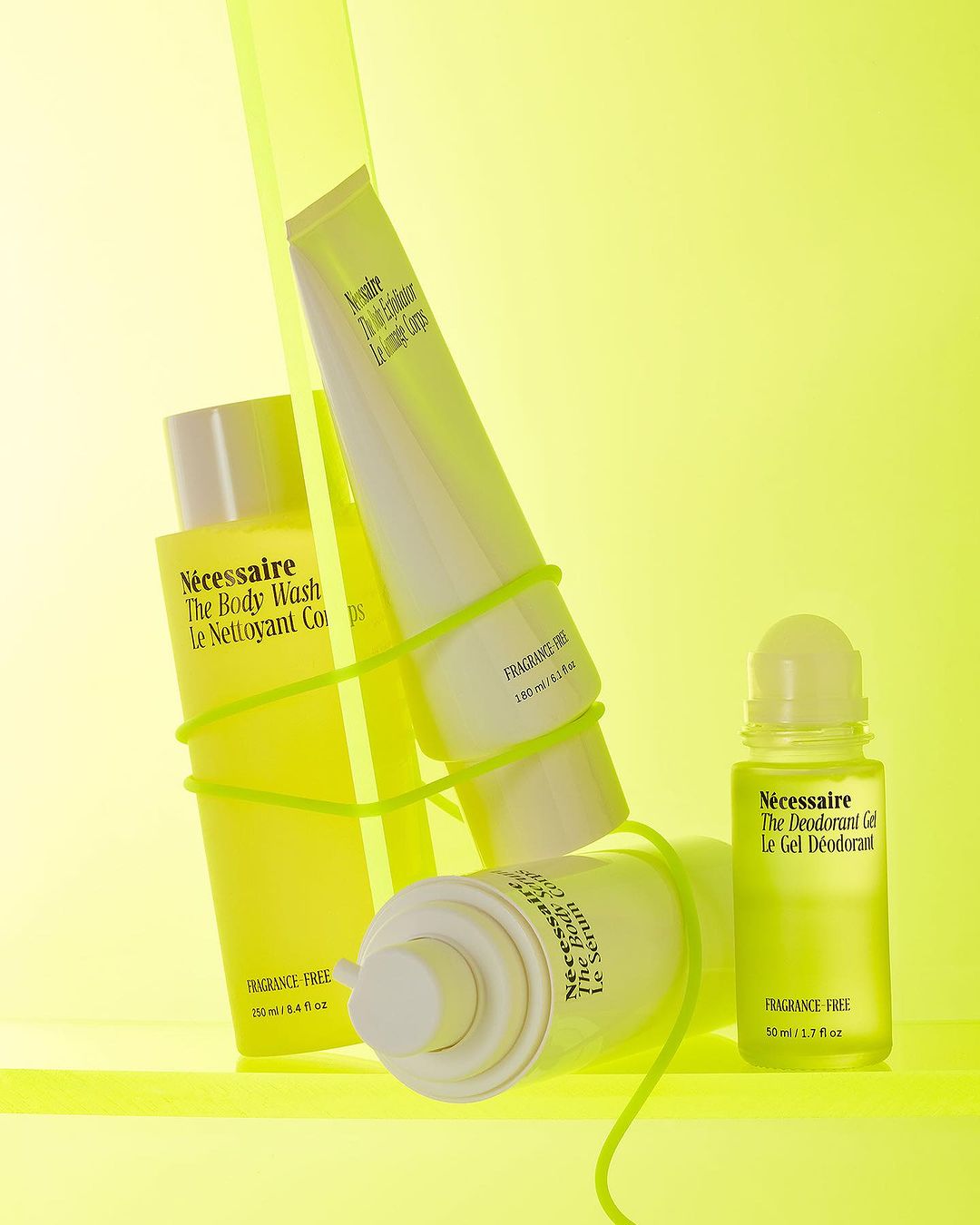 Cosmetic product bottles and containers including body wash and deodorant arranged on a vivid yellow surface with bright lighting.