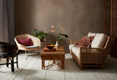 Styled interior living space with a woven rattan sofa, matching coffee table with floral vase, wicker armchair, and textured rug.