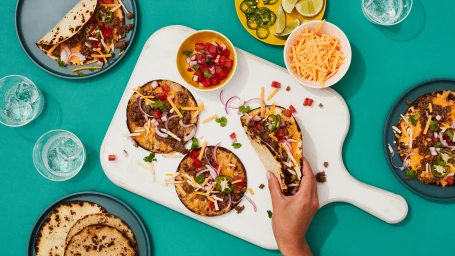 Overhead food photography of tacos on a white cutting board and plates with a turquoise background