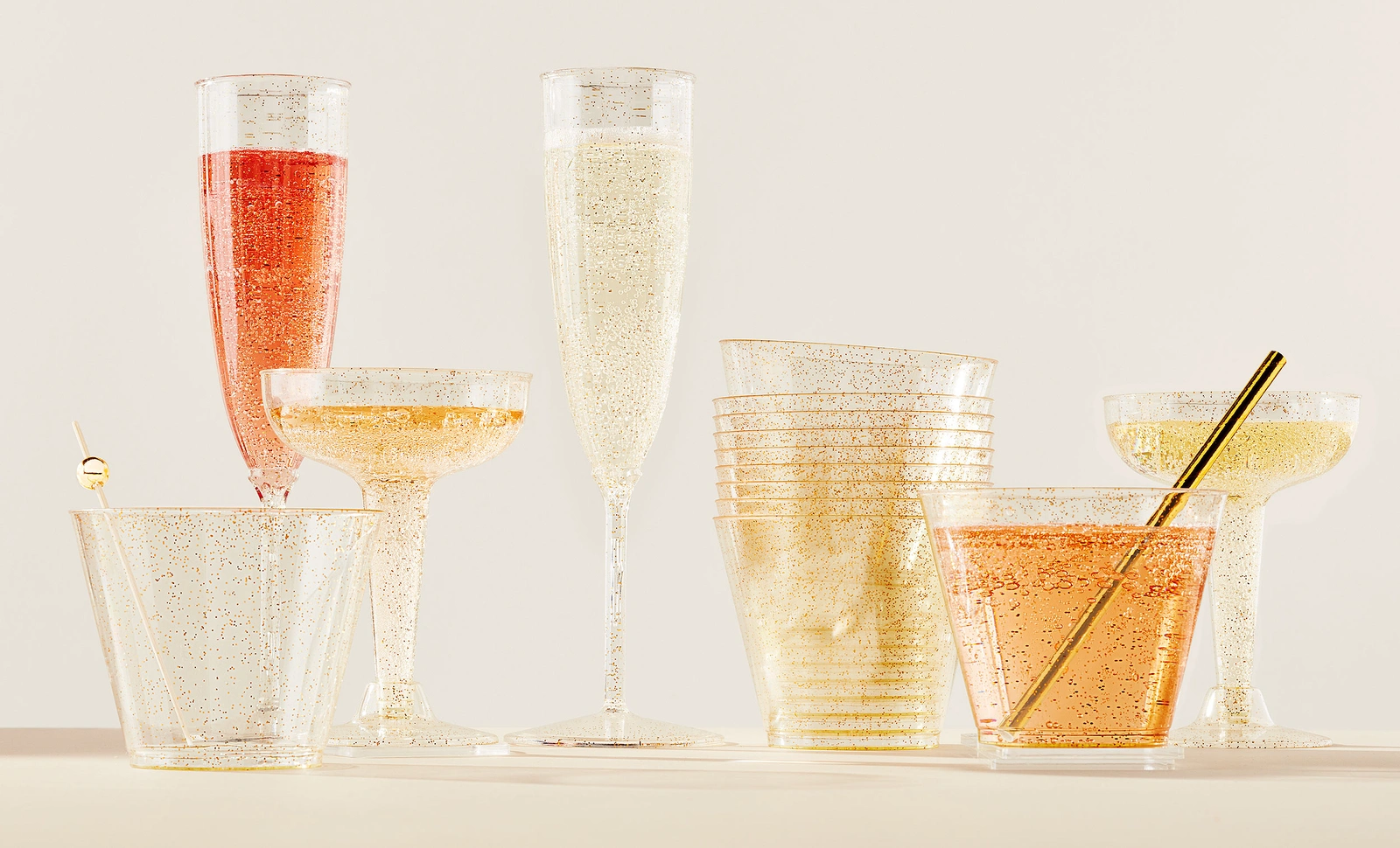 A collection of plastic champagne flutes, coupes, and tumblers with gold glitter details against a neutral background.
