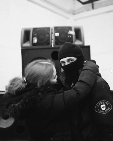 Monochrome shot of a woman and a man with a balaclava with speakers in the background, close up shot.